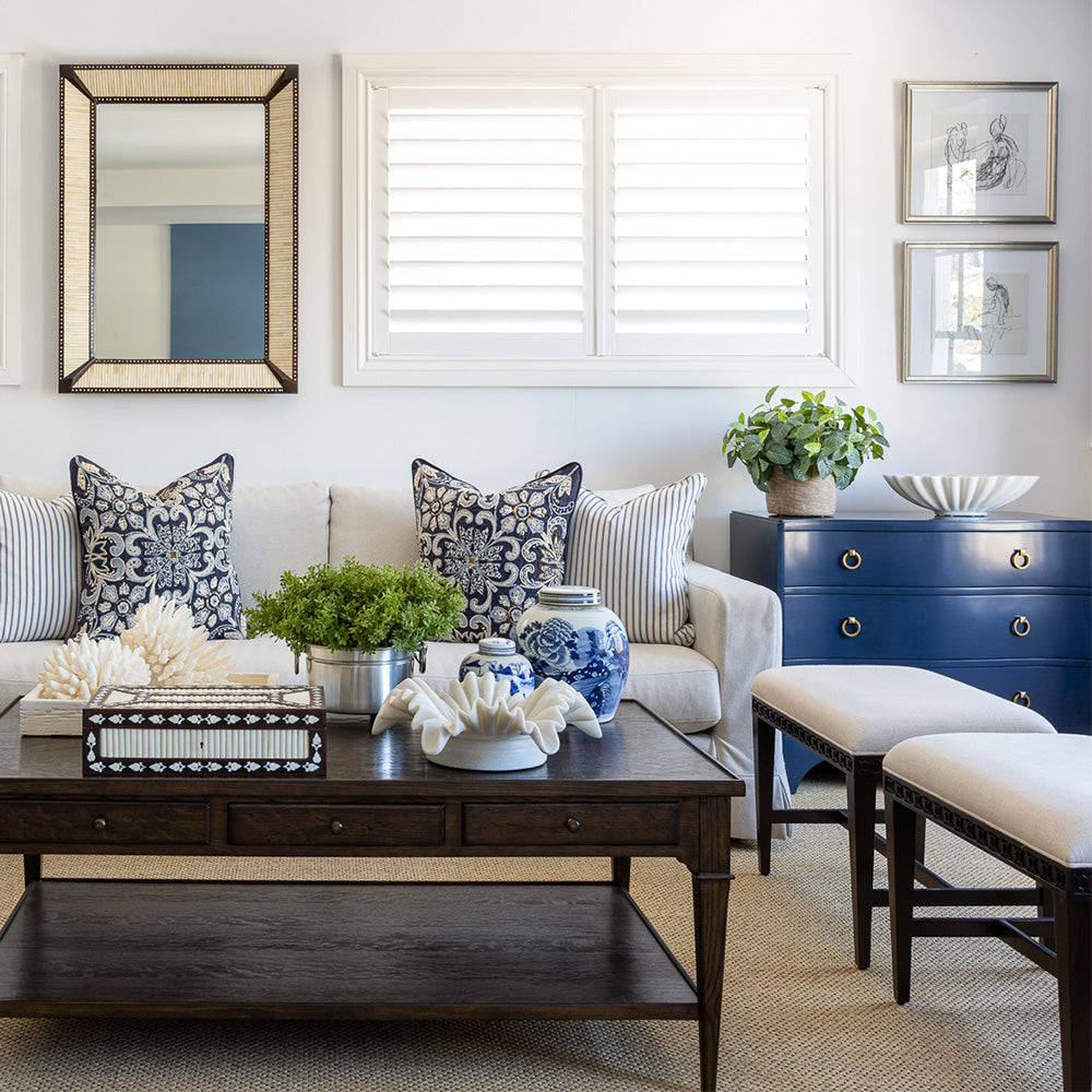 Huxley coffee table styled in front of a neutral sofa with navy embroidered and navy and white striped cushions. The coffee table is styled with a wooden bone inlay box, a ruffled marble bowl, two small blue and white ginger jars, a faux greenery arrangement and a carved bone inlay tray with decorative coral.