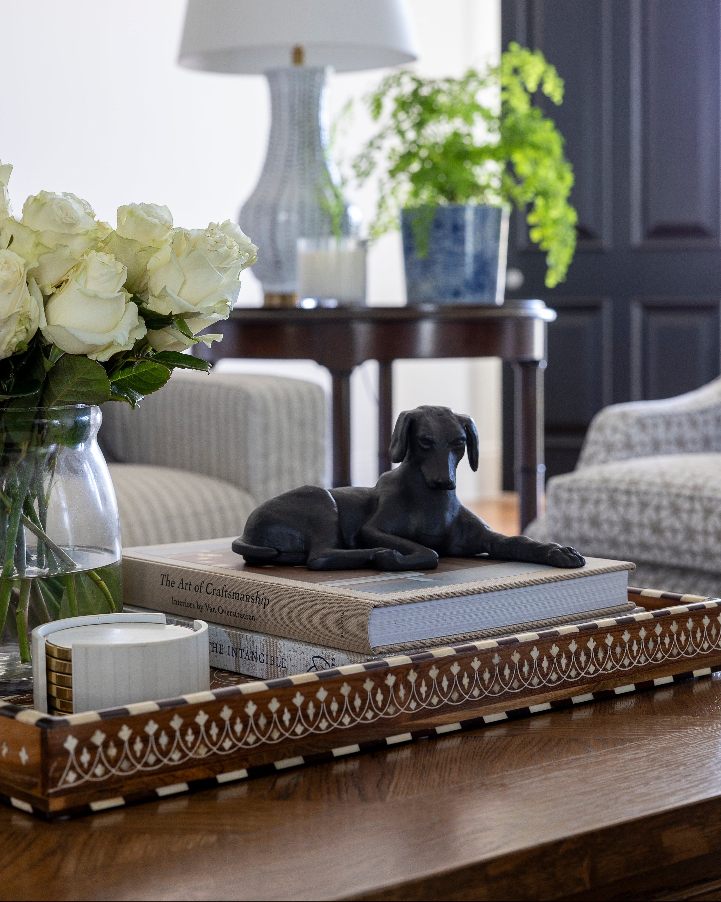 Decorative tray with a black dog figurine, books, and flowers on a wooden surface.