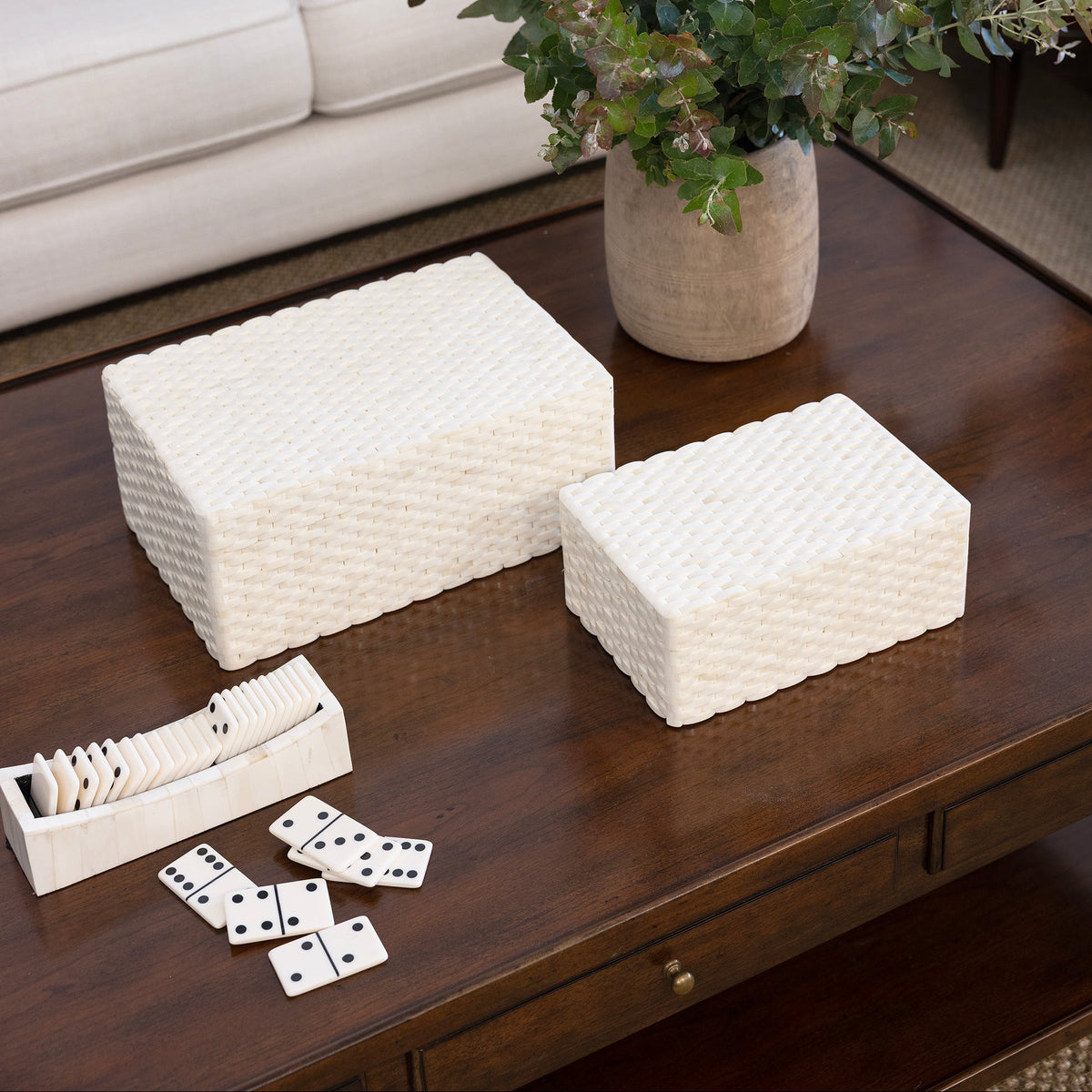 Decorative boxes on a coffee table with a vase of flowers and dominoes in a living room setting.