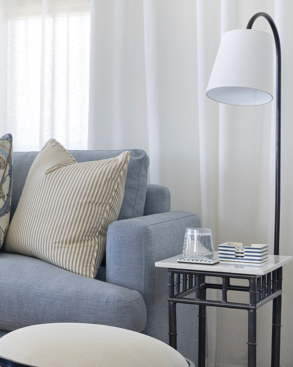 A modern living room corner featuring a light blue sofa with striped throw pillows, a black floor lamp with a white drum shade, and a small side table.