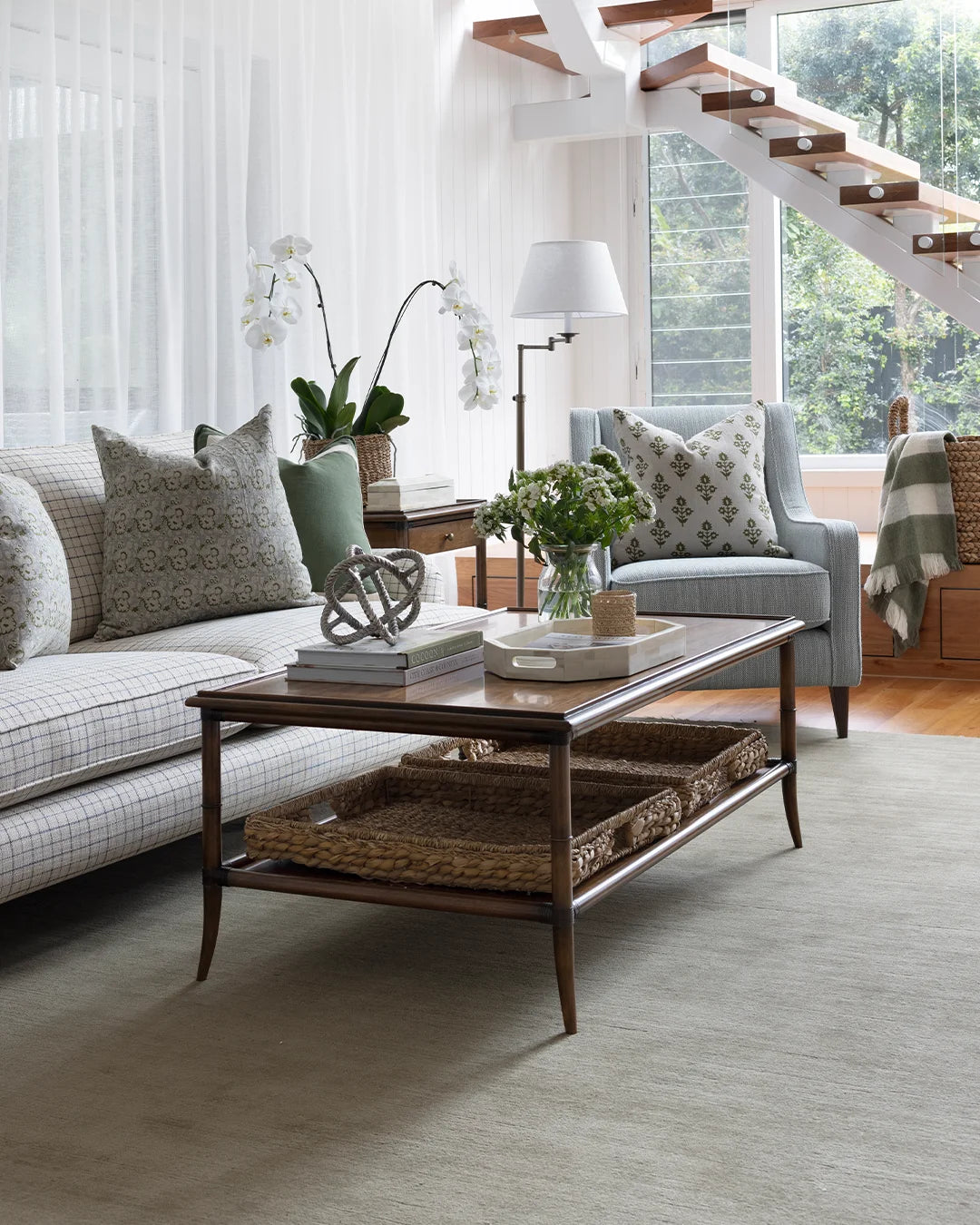 Lydia Coffee table in centre of room, styled with flowers, a tray and books topped with decorative knot. Green rug, with checked sofa and blue occasional chair.