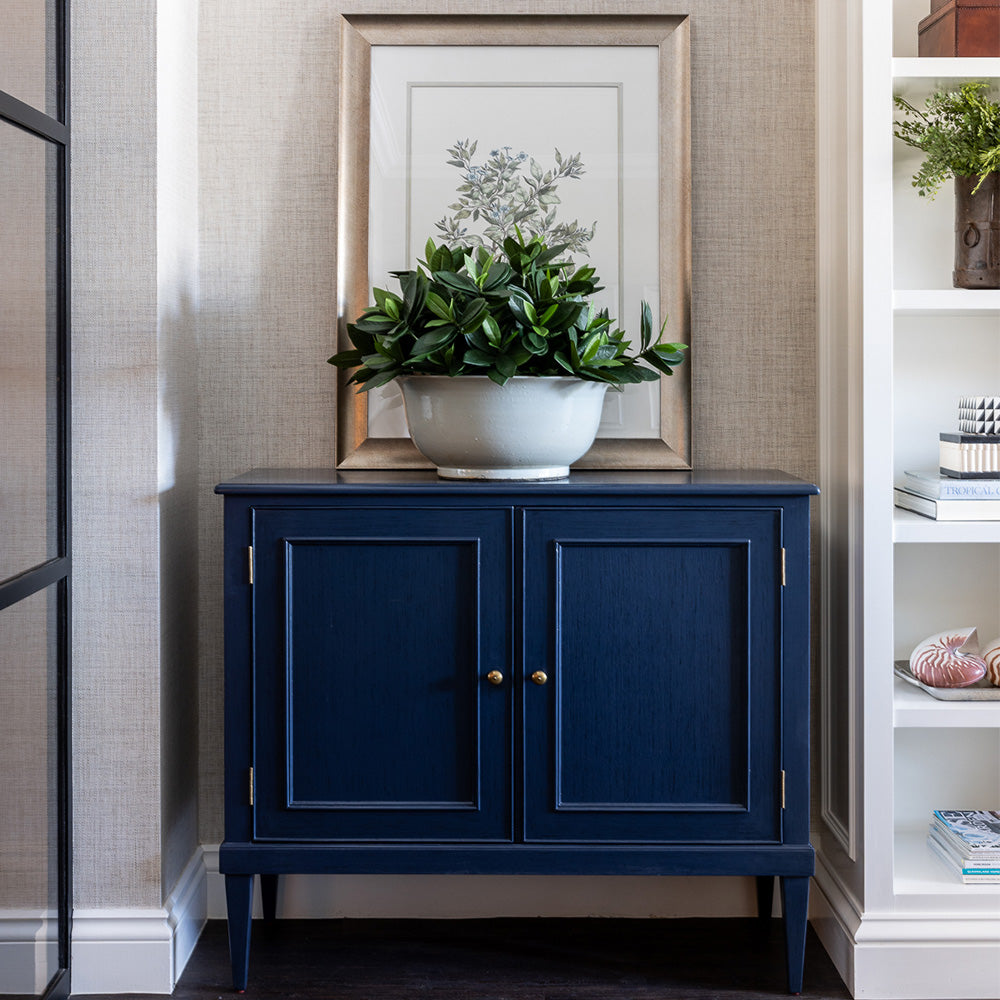 Navy Toulon Hall chest styled next to a built in bookcase. A large white bowl with faux sweet leaf greenery and an artwork placed behind.