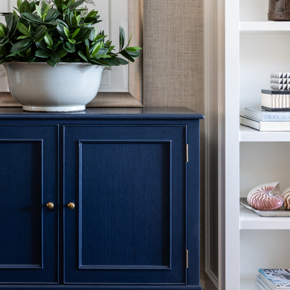 Navy Toulon Hall chest styled next to a built in bookcase. A large white bowl with faux sweet leaf greenery and an artwork placed behind. Close up image