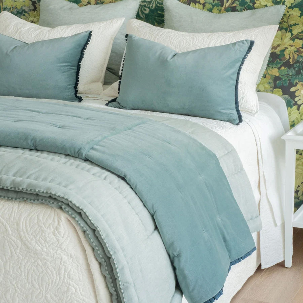 Bed styled with white quilt and two white pillows, duck egg euros behind and two blue velvet lumbers in front. Blue velvet comforter folded at bed end, with lighter duck egg quilt underneath.