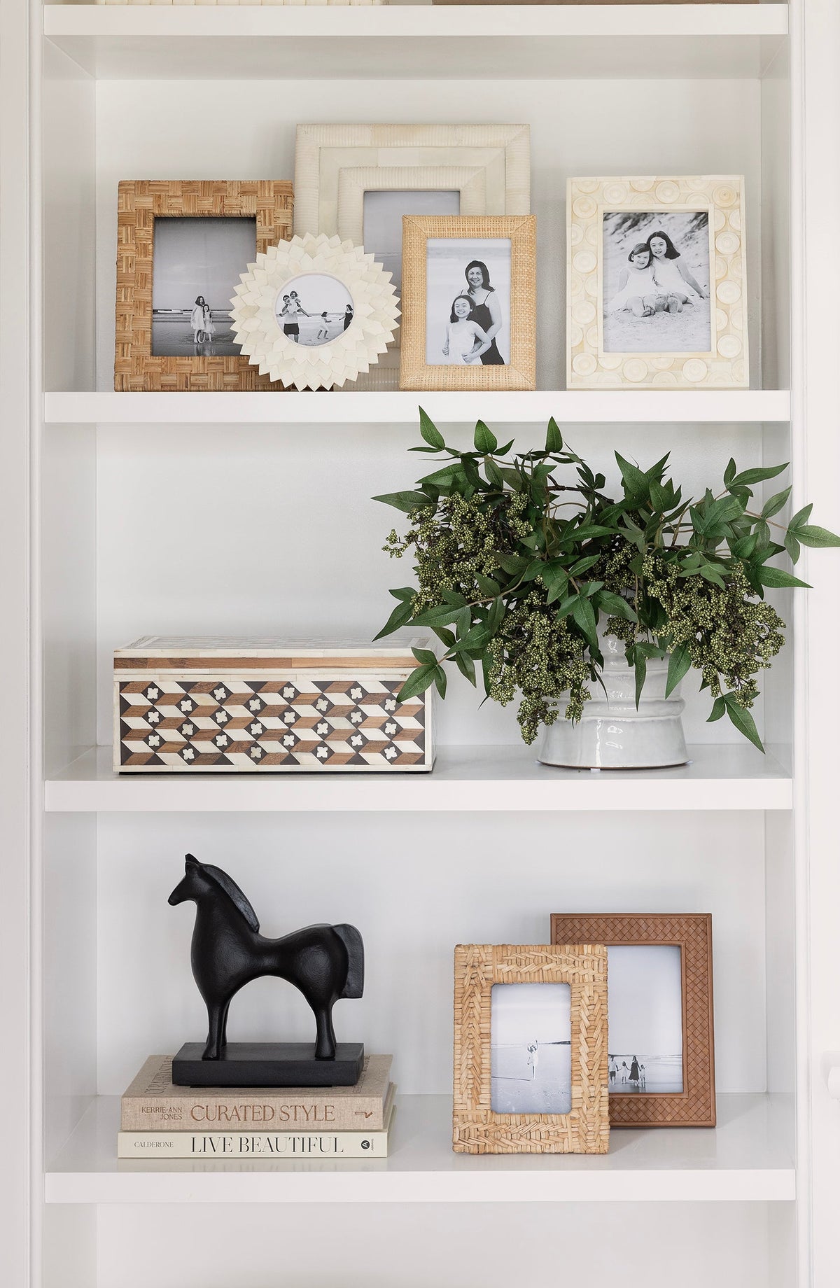 Decorative bookshelf with framed photos, plants, and sculptures.