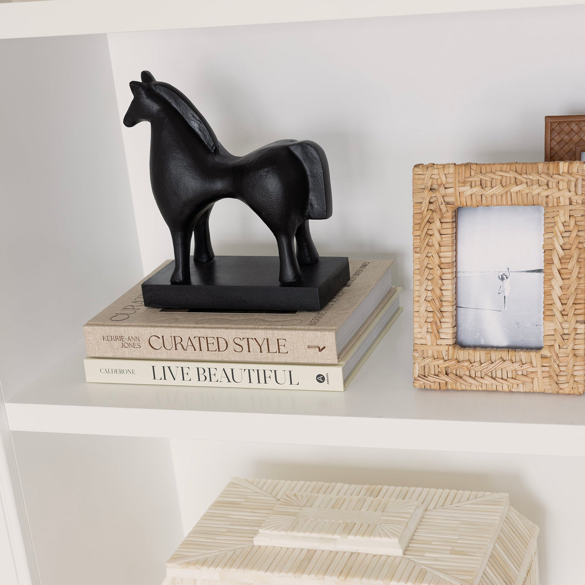 Decorative shelf with a black horse figurine, books, and a woven box.