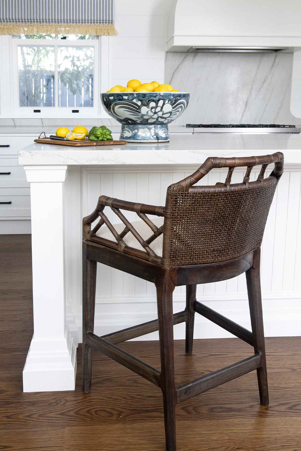 dark rattan bar stool in a kitchen setting with a bowl of fruit on the counter.