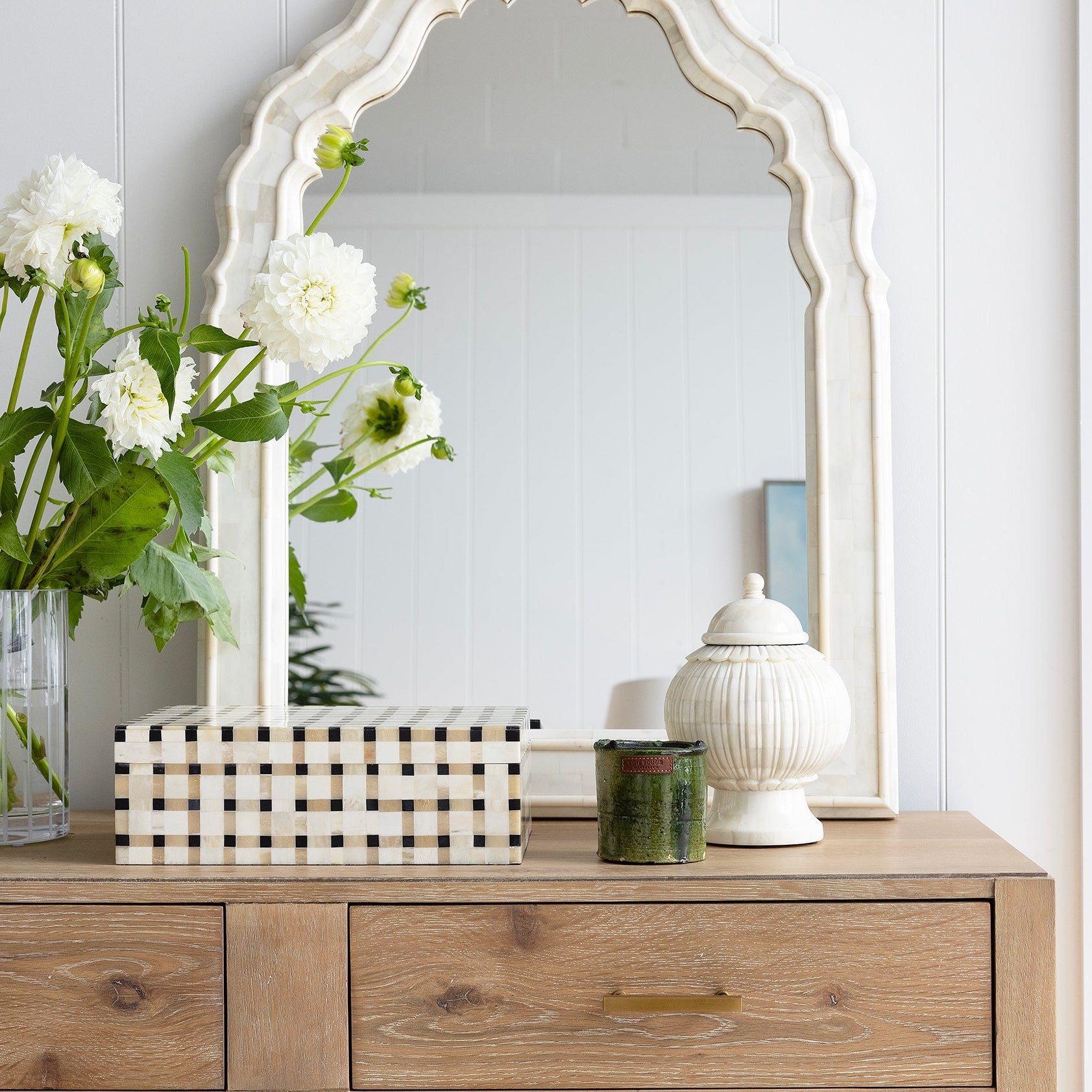 Wooden dresser with decorative items and a large mirror against a white wall.