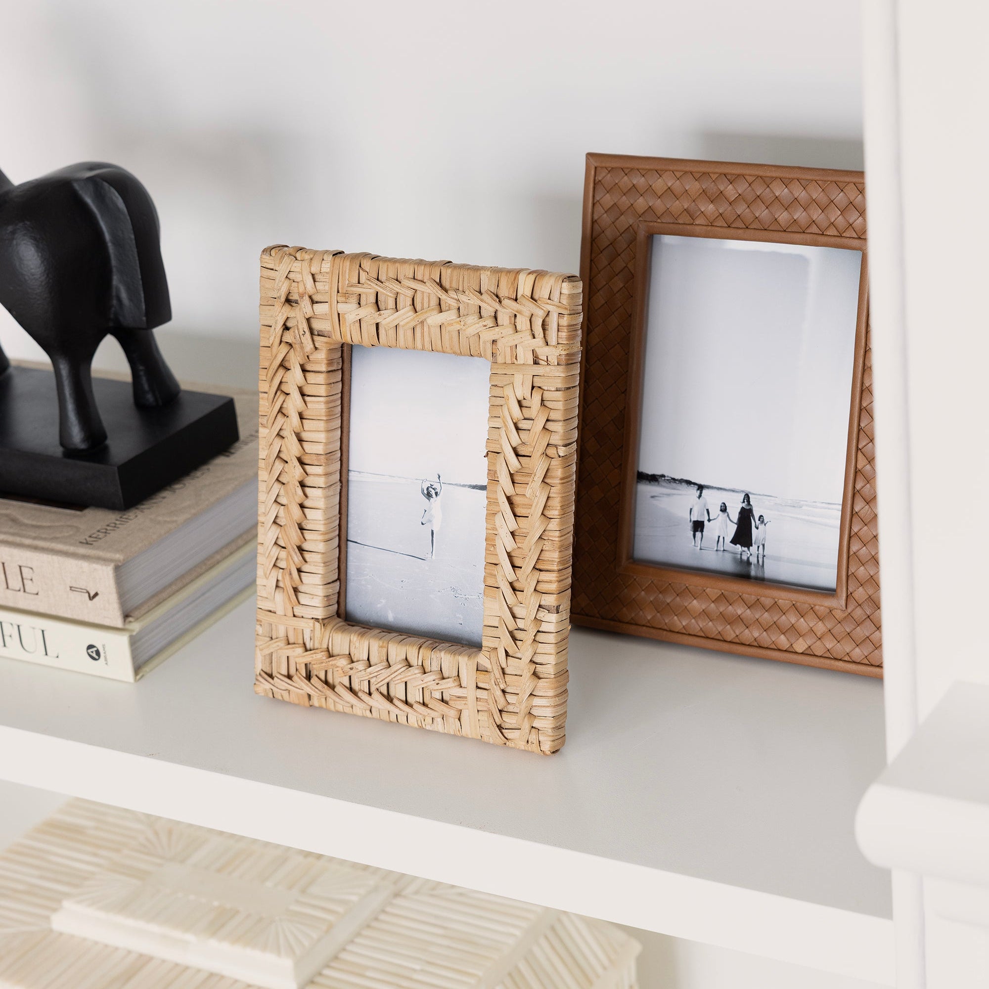 Two wicker picture frames on a white shelf with books and a decorative object.