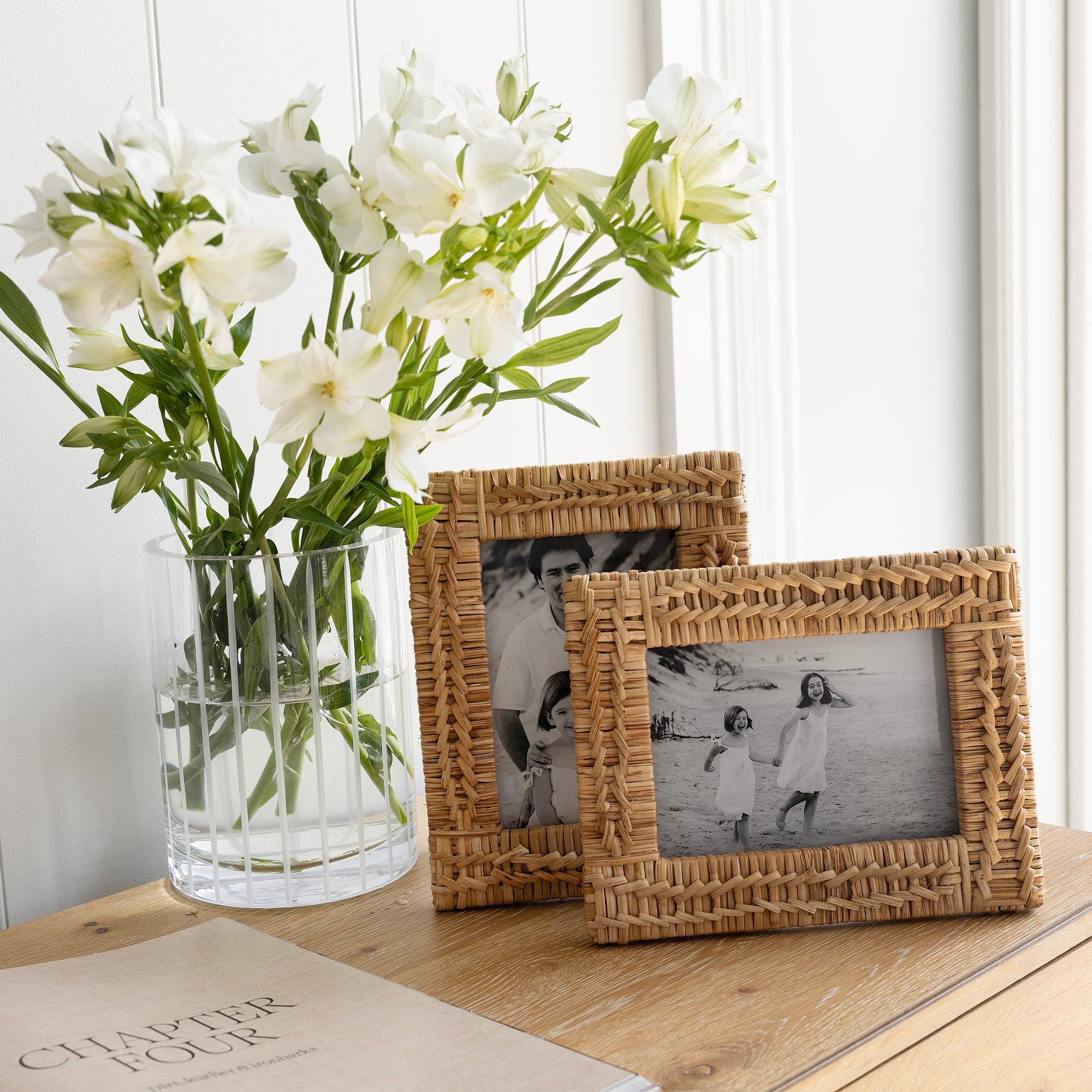 Wicker picture frames and a vase with white flowers on a wooden surface.