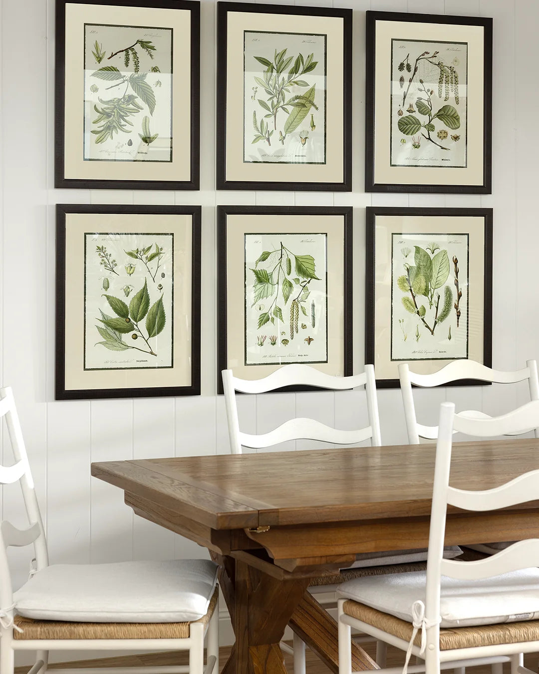 Six green plant print artworks arranged in grid on white vj back wall. Dining table with white wavy chairs in front.