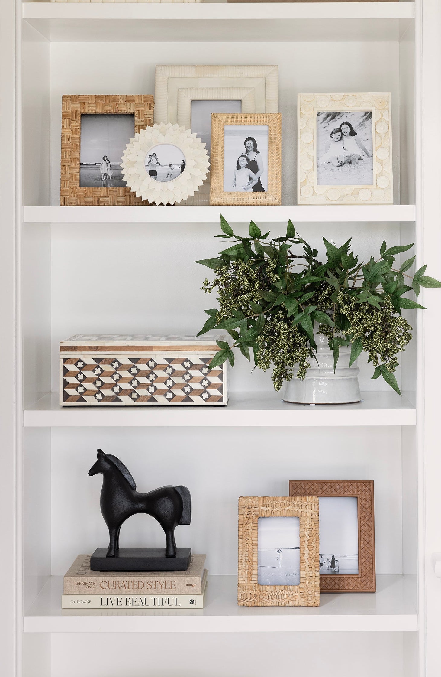 Decorative bookshelf with framed photos, plants, and sculptures.
